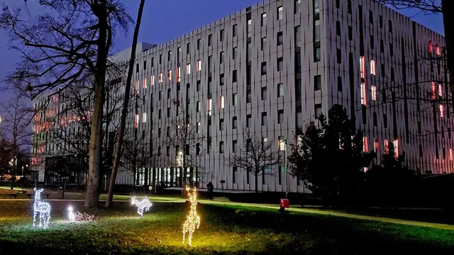 Großes, modernes Bürogebäude mit beleuchteten Fenstern bei Nacht, davor leuchtende Rentierfiguren auf einer Wiese mit Bäumen.