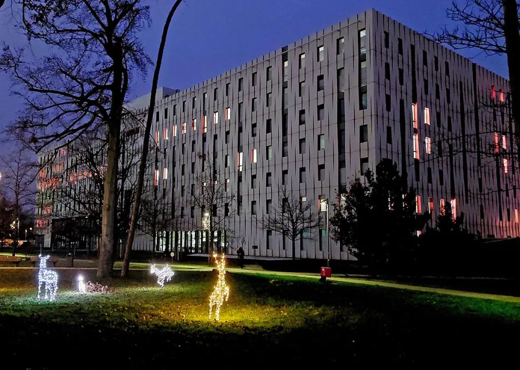 Großes, modernes Bürogebäude mit beleuchteten Fenstern bei Nacht, davor leuchtende Rentierfiguren auf einer Wiese mit Bäumen.