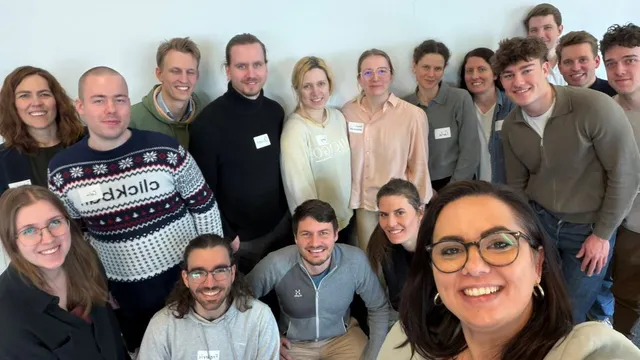 Gruppe von Menschen mit Namensschildern steht vor weißer Wand und schaut in die Kamera