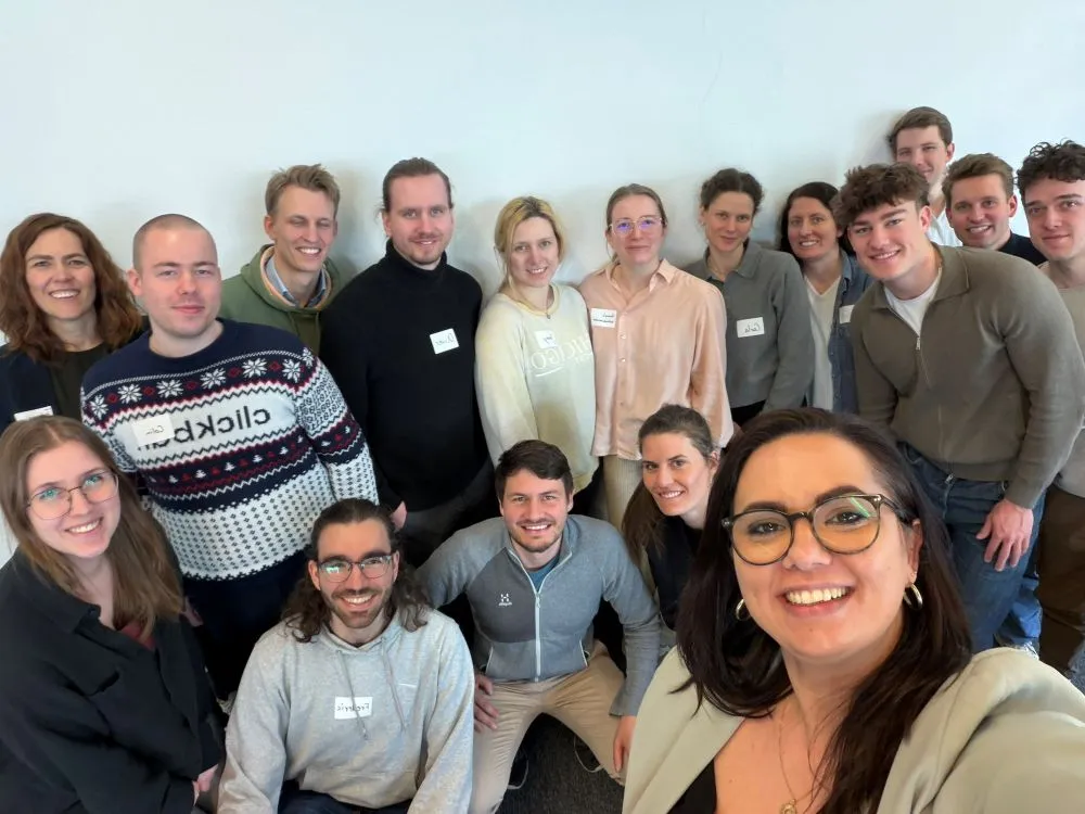 Gruppe von Menschen mit Namensschildern steht vor weißer Wand und schaut in die Kamera