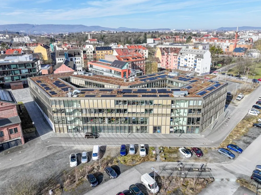 Luftaufnahme eines modernen Bürogebäudes mit Glasfassade in Kassel, umgeben von Parkplätzen und Wohnhäusern