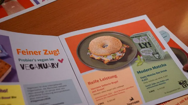 Aufgeschlagene Broschüre mit einem Bagel auf einem Teller und Texten zu veganem Angebot und Matcha-Getränk