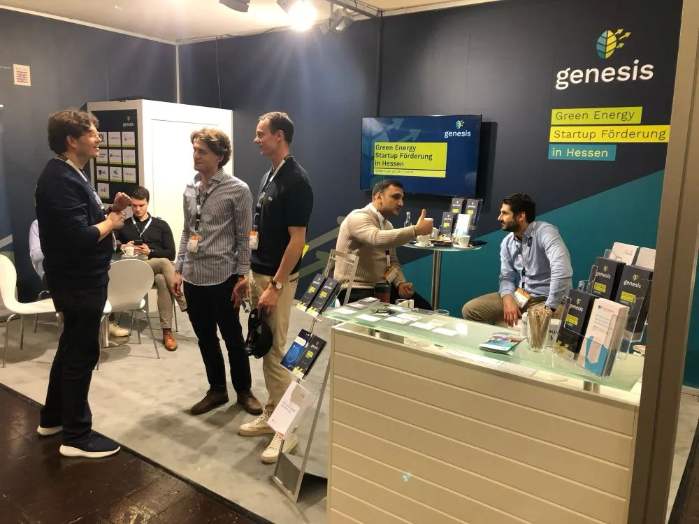 Messestand mit fünf Personen, Informationsmaterial auf Theke und Wand mit Schriftzug 'genesis Green Energy Startup Förderung in Hessen'