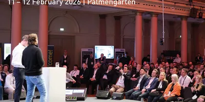 Zwei Männer stehen auf einer Bühne vor einem Publikum in einem großen, historischen Saal mit hohen Säulen und einer Galerie. Über der Szene steht in großen Buchstaben 'FRANKFURT DIGITAL FINANCE' und 'EuropeanFintechDay' mit dem Datum '11 – 12 February.