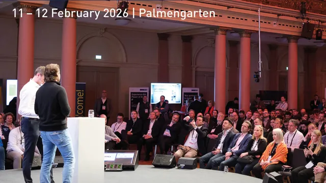 Zwei Männer stehen auf einer Bühne vor einem Publikum in einem großen, historischen Saal mit hohen Säulen und einer Galerie. Über der Szene steht in großen Buchstaben 'FRANKFURT DIGITAL FINANCE' und 'EuropeanFintechDay' mit dem Datum '11 – 12 February.