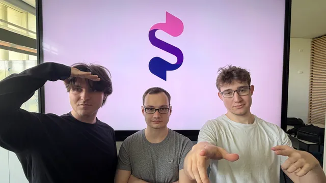 Drei junge Männer vor einem Bildschirm mit einem stilisierten S-Logo, einer grüßt mit der Hand an der Stirn, die anderen zwei zeigen mit den Händen nach vorne