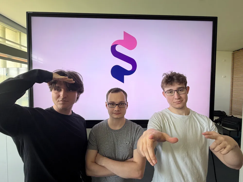 Drei junge Männer vor einem Bildschirm mit einem stilisierten S-Logo, einer grüßt mit der Hand an der Stirn, die anderen zwei zeigen mit den Händen nach vorne