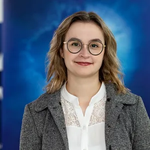 Friederike Lenke, eine Frau mit schulterlangen, gewellten Haaren trägt grauen Blazer und weiße Bluse mit Spitzenmuster im Brustbereich.