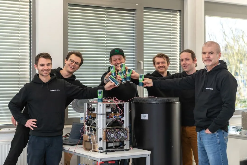 Fünf Personen in schwarzer und blauer Kleidung stehen um technische Geräte und stoßen Dosen an.