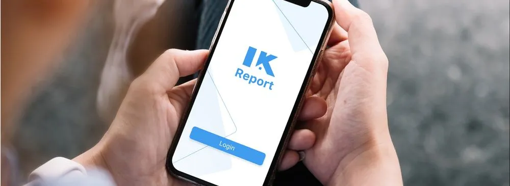 Person hält Smartphone mit geöffneter App, auf dem Bildschirm steht 'IK Report' und ein blauer Login-Button