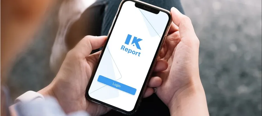 Person hält Smartphone mit geöffneter App, auf dem Bildschirm steht 'IK Report' und ein blauer Login-Button
