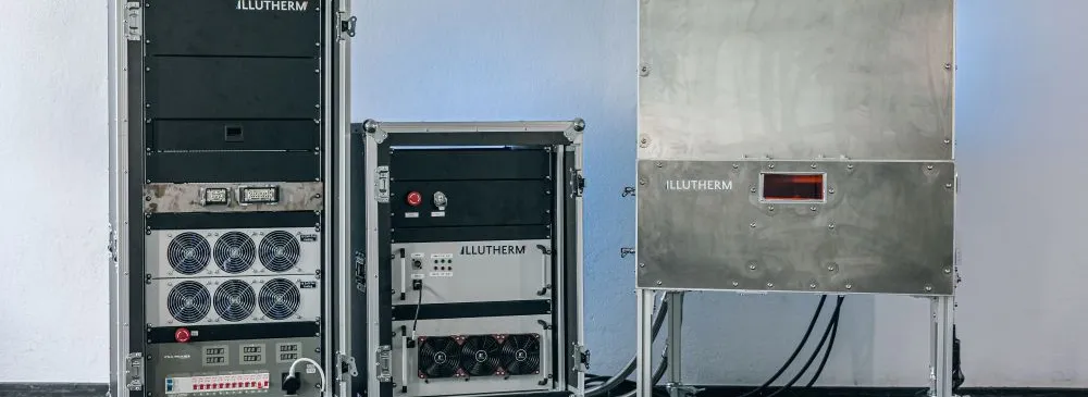 Drei verschiedene technische Geräte mit dem Schriftzug 'ILLUTHERM' auf Rollen in einem Raum mit grauer Wand und dunklem Boden