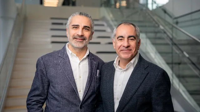 Zwei Männer in Anzügen stehen vor einer Treppe in einem modernen Gebäude