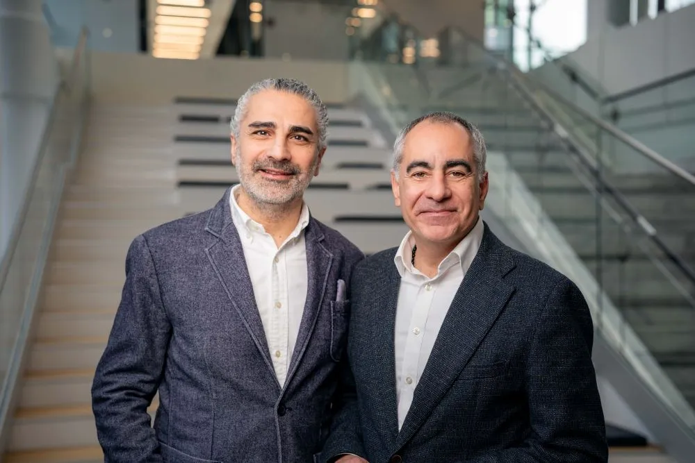 Zwei Männer in Anzügen stehen vor einer Treppe in einem modernen Gebäude