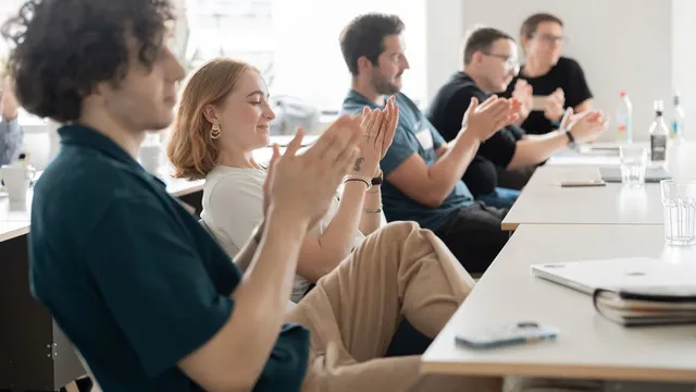 Mehrere Personen sitzen an einem Tisch und klatschen mit sichtbaren Händen und Oberkörpern.