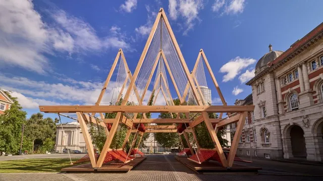 Holzkonstruktion mit dreieckigen Rahmen und roten Hängematten auf gepflastertem Platz beim London Design Festival