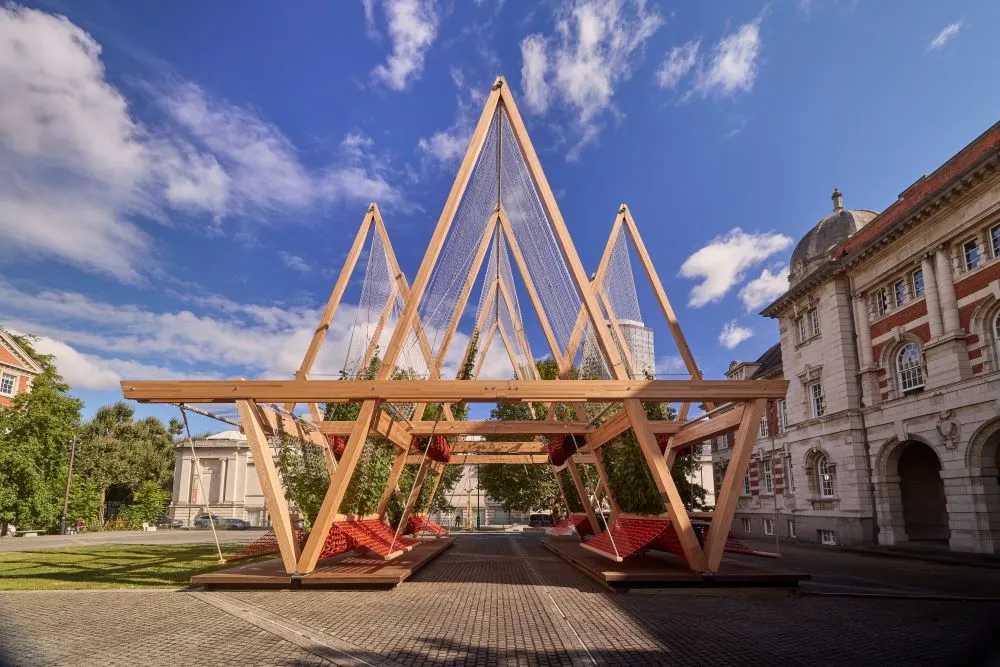 Holzkonstruktion mit dreieckigen Rahmen und roten Hängematten auf gepflastertem Platz beim London Design Festival