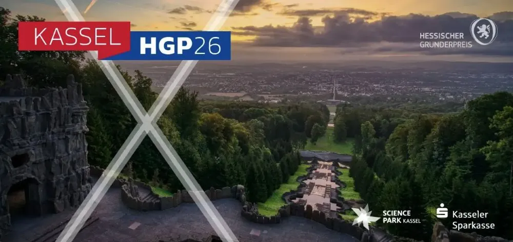 Blick vom Herkules auf Kassel mit Stadtpanorama und grünen Parkanlagen im Vordergrund, darüber ein rotes Banner mit weißer Schrift 'KASSEL' und ein blaues Banner mit weißer Schrift 'HGP26'