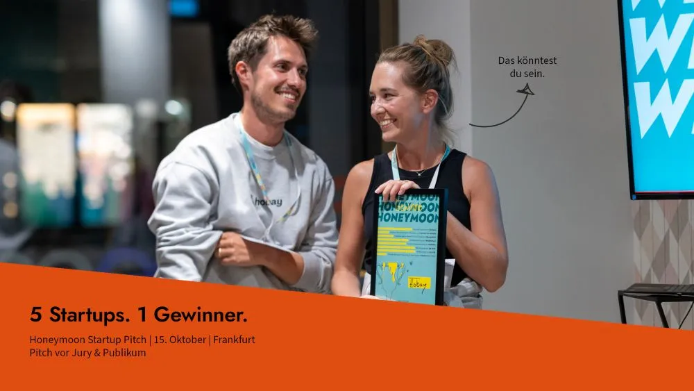 Zwei lächelnde Personen sitzen an einem Tisch, eine hält ein Buch mit dem Titel 'HONEYMOON', daneben steht der Text '5 Startups. 1 Gewinner. Honeymoon Startup Pitch | 15. Oktober | Frankfurt Pitch vor Jury & Publikum'