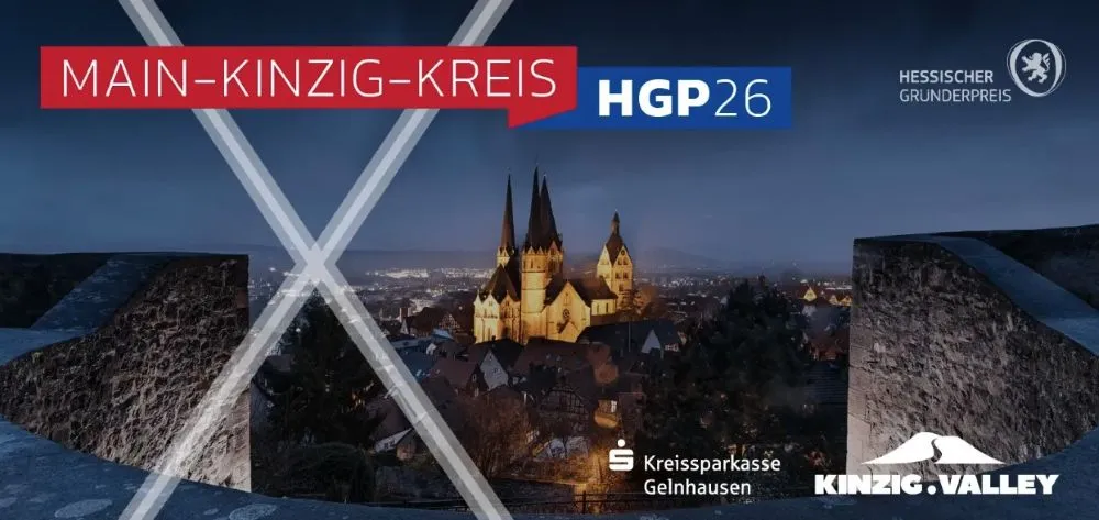 Nachtaufnahme einer Stadt mit einer beleuchteten Kirche und zwei hohen Türmen, im Vordergrund zwei beleuchtete, sich kreuzende Stahlträger, darüber rote und blaue Banner mit den Schriftzügen 'MAIN-KINZIG-KREIS' und 'HGP26' sowie Logos von 'Kreissparkasse