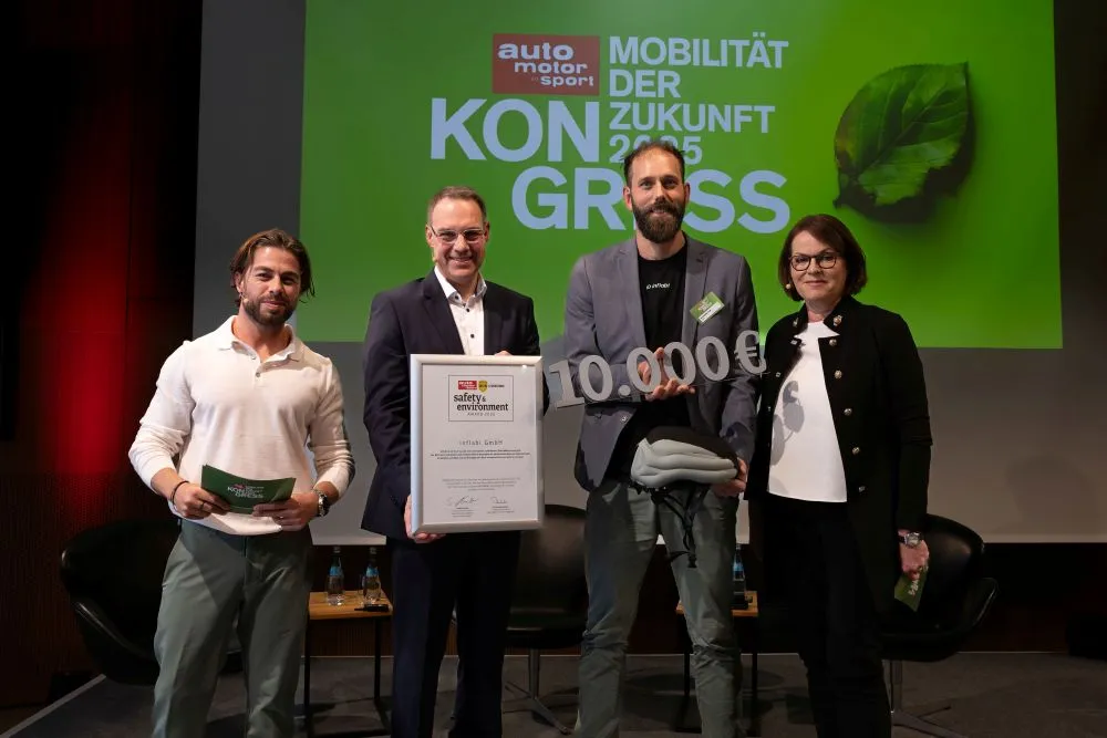 Vier Personen stehen vor einer grünen Leinwand mit dem Text 'auto motor sport MOBILITÄT DER ZUKUNFT 2025 KONGRESS'. Eine Person hält eine Urkunde, eine andere ein Schild mit '10.000 €.