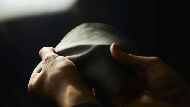 Zwei Hände halten ein weiches, dunkles, rechteckiges Materialstück in gedämpftem Licht