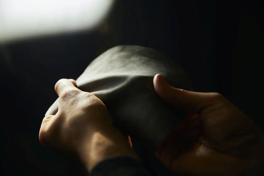 Zwei Hände halten ein weiches, dunkles, rechteckiges Materialstück in gedämpftem Licht