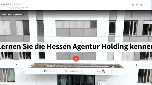 Fassade eines modernen Bürogebäudes mit großen Fenstern und Textbanner 'Lernen Sie die Hessen Agentur Holding kennen' in schwarzer Schrift auf weißem Hintergrund.