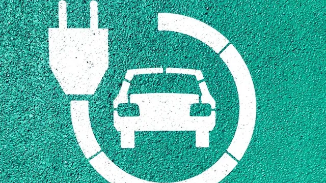 Weißes Piktogramm eines Autos mit Ladestecker auf grünem Asphalt