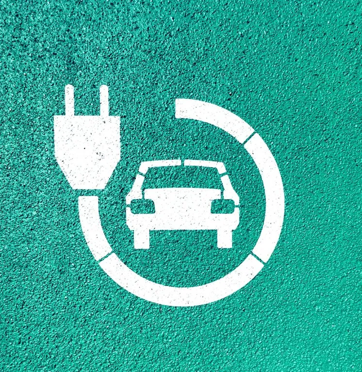 Weißes Piktogramm eines Autos mit Ladestecker auf grünem Asphalt
