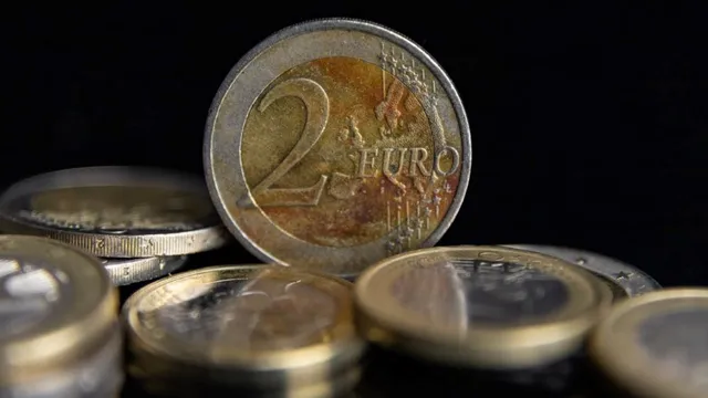 Nahaufnahme einer 2-Euro-Münze stehend vor mehreren liegenden Euro-Münzen