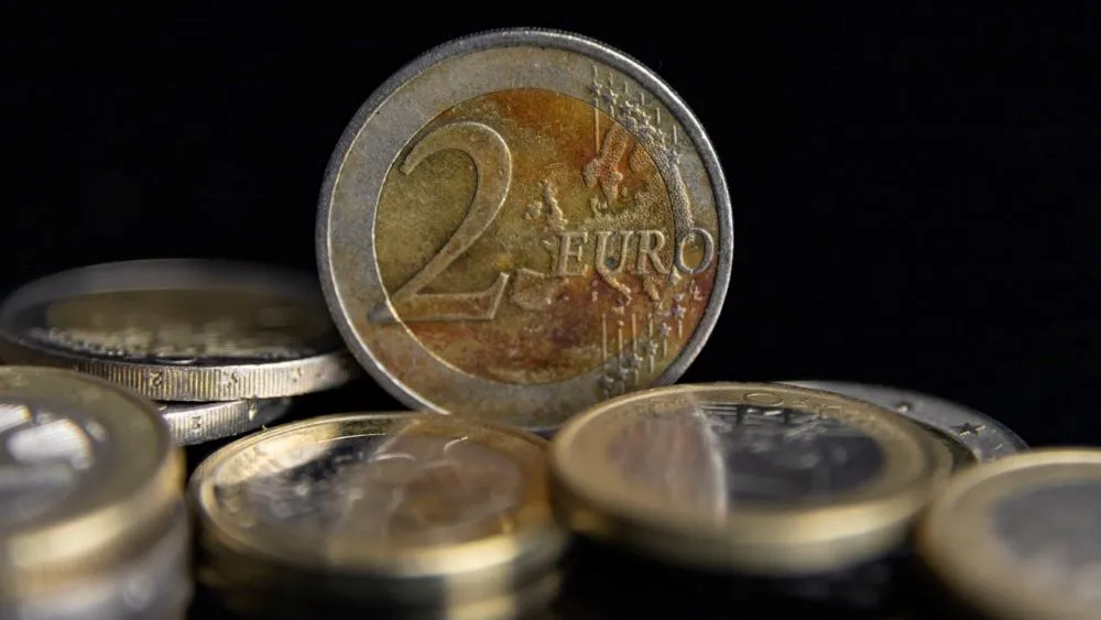 Nahaufnahme einer 2-Euro-Münze stehend vor mehreren liegenden Euro-Münzen