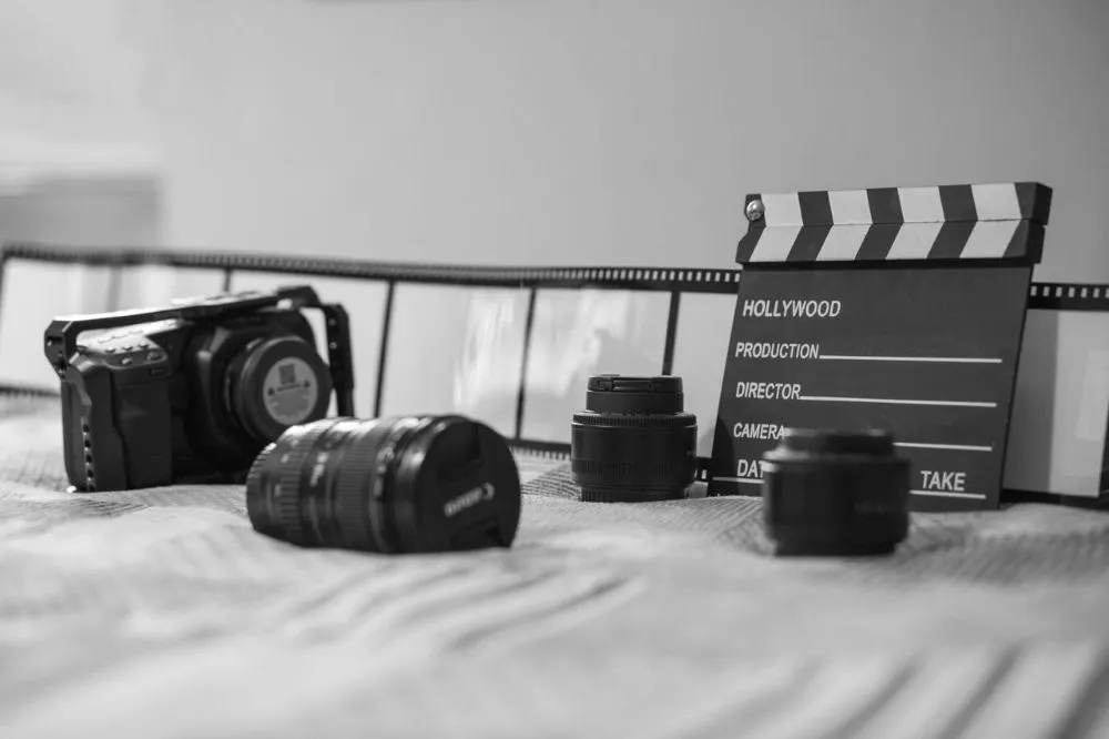 Schwarz-weiße Nahaufnahme von Filmkamera, Kameraobjektiven, Filmklappe und Filmstreifen auf einer Oberfläche