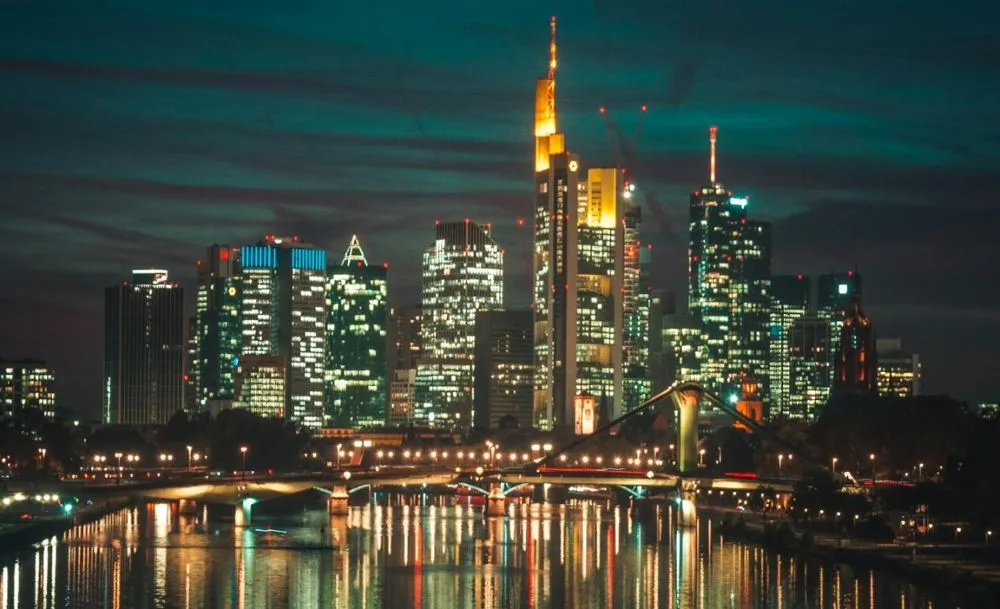 Nächtliche Skyline von Frankfurt mit beleuchteten Hochhäusern und Brücke über den Fluss