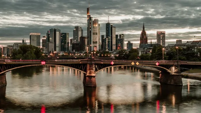 Blick auf die Frankfurter Skyline mit Hochhäusern und einer Brücke über den Main bei bewölktem Himmel
