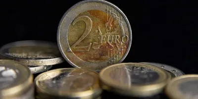 Nahaufnahme einer 2-Euro-Münze stehend vor mehreren liegenden Euro-Münzen auf dunklem Hintergrund