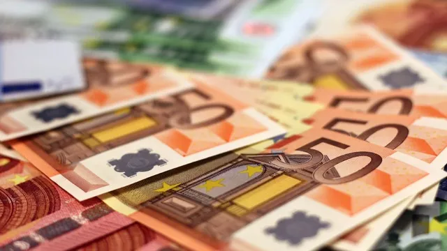 Mehrere 50-Euro-Scheine liegen übereinander, im Hintergrund unscharfe Euro-Banknoten verschiedener Werte.