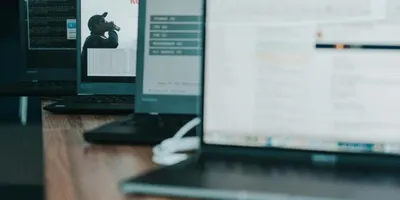 Mehrere Laptops auf einem Holztisch, auf einem Bildschirm ist eine Person mit Kamera zu sehen