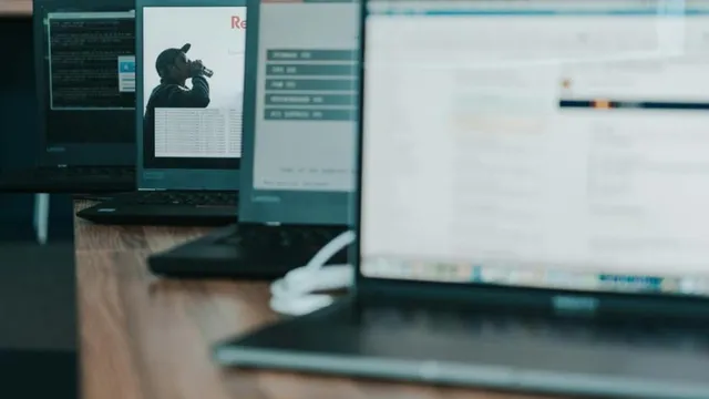 Mehrere Laptops auf einem Holztisch, auf einem Bildschirm ist eine Person mit Kamera zu sehen