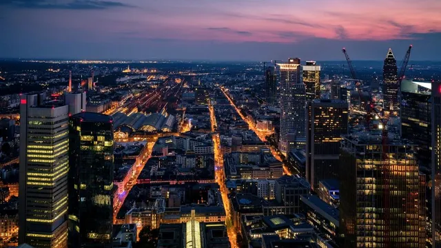 Blick auf die Skyline von Frankfurt am Main bei Dämmerung, mit beleuchteten Straßen und Wolkenkratzern, darunter der Hauptbahnhof.