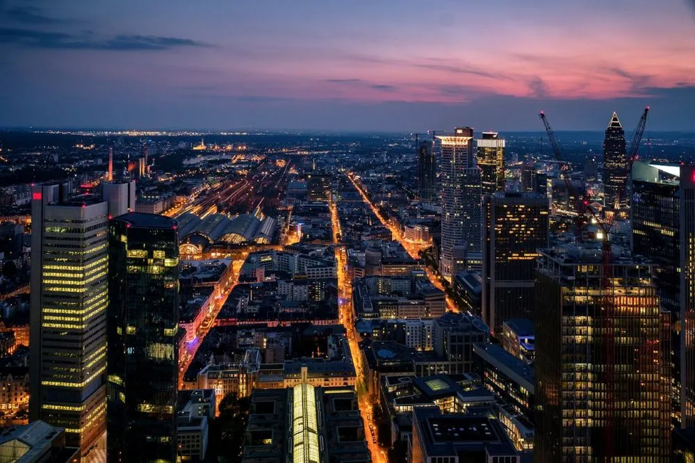 Blick auf die Skyline von Frankfurt am Main bei Dämmerung, mit beleuchteten Straßen und Wolkenkratzern, darunter der Hauptbahnhof.