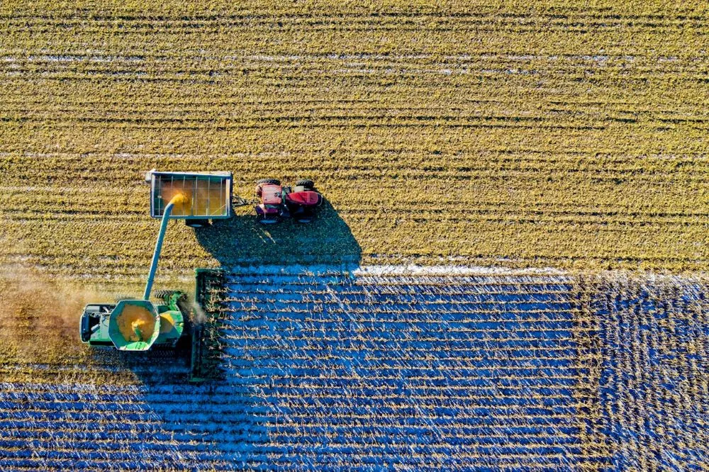 Luftaufnahme von zwei landwirtschaftlichen Fahrzeugen auf einem Feld, die Erntegut in einen Anhänger laden