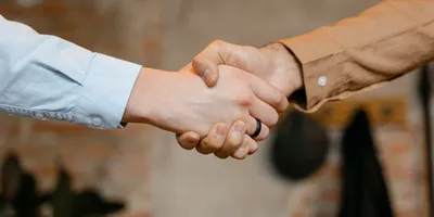 Zwei Personen geben sich die Hand, eine trägt ein hellblaues Hemd, die andere ein braunes Hemd