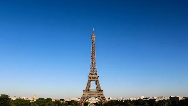 Eiffelturm in Paris vor klarem Himmel, umgeben von Stadt und Bäumen.