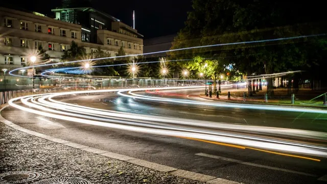 Lichtspuren von Fahrzeugen auf einer kurvigen Straße in einer nächtlichen Stadtlandschaft