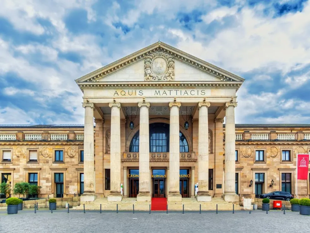 Fassade eines historischen Gebäudes mit Säulen und der Inschrift 'AQUIS MATTIACIS' unter blauem Himmel