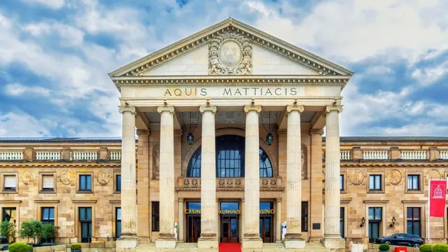 Fassade eines historischen Gebäudes mit Säulen und der Inschrift 'AQUIS MATTIACIS' unter blauem Himmel