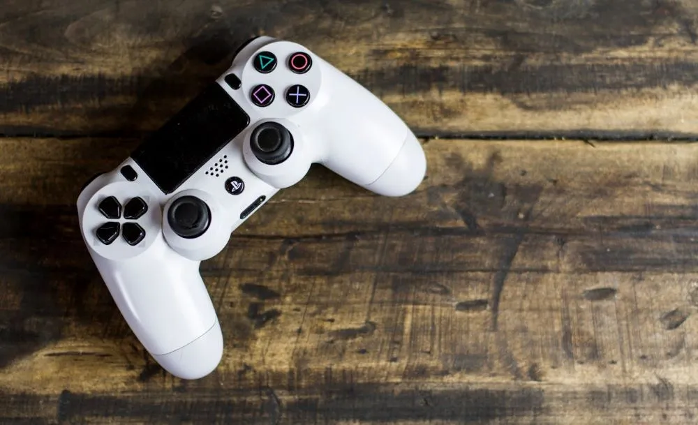 Weißer PlayStation-Controller mit schwarzen Tasten auf rustikalem Holztisch