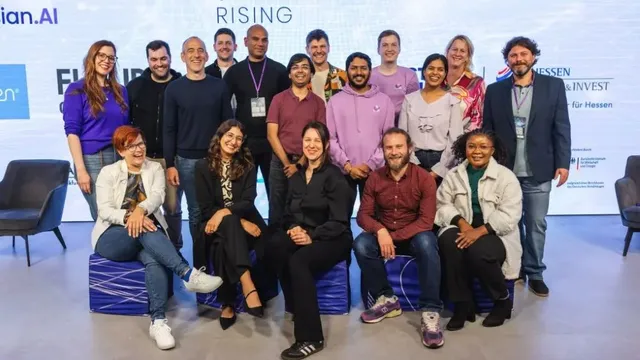 Gruppe von Menschen in legerer Kleidung vor einer Wand mit dem Schriftzug 'AI STARTUP RISING'