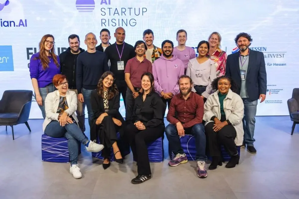 Gruppe von Menschen in legerer Kleidung vor einer Wand mit dem Schriftzug 'AI STARTUP RISING'